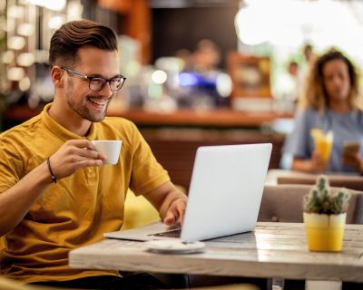 Happy man surfing the Internet on coffee break in a cafe.